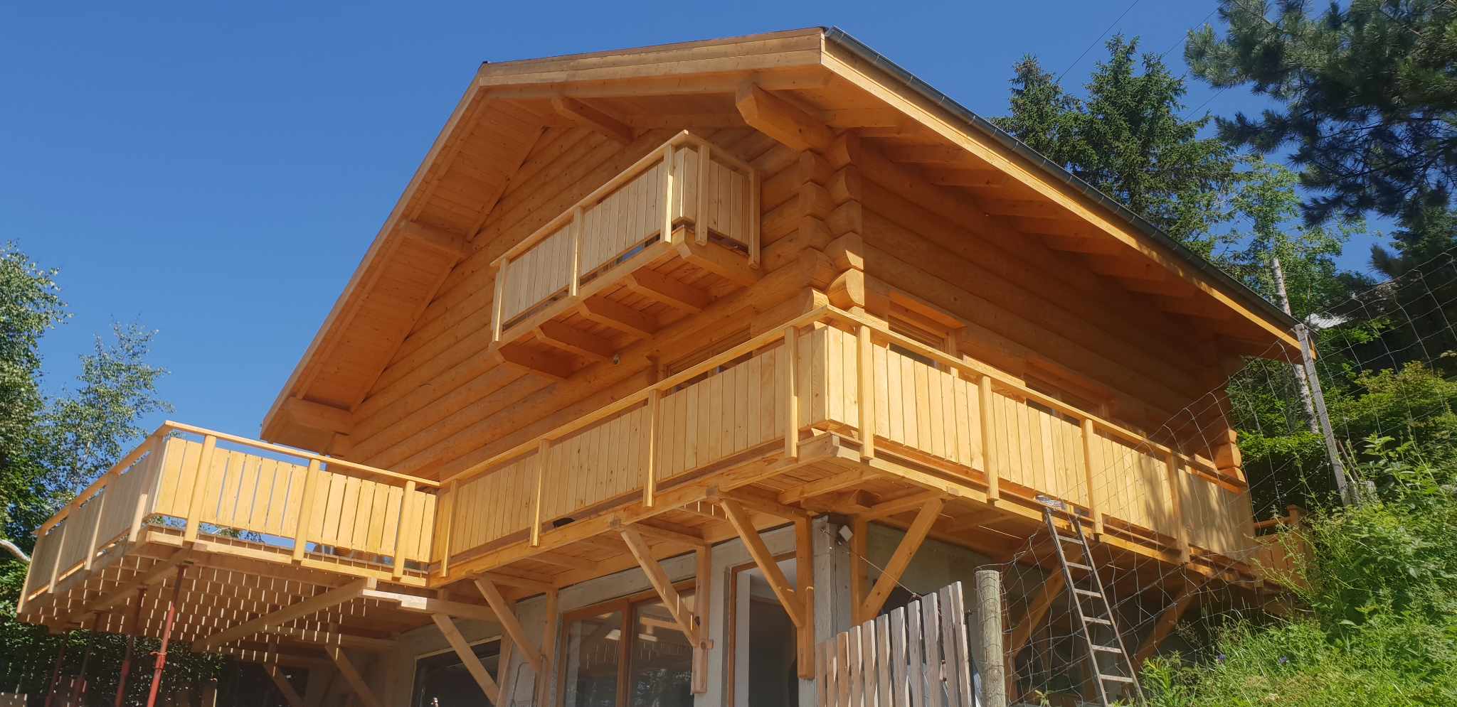 Blockhaus mit umlaufendem Holzbalkon vor blauem Himmel